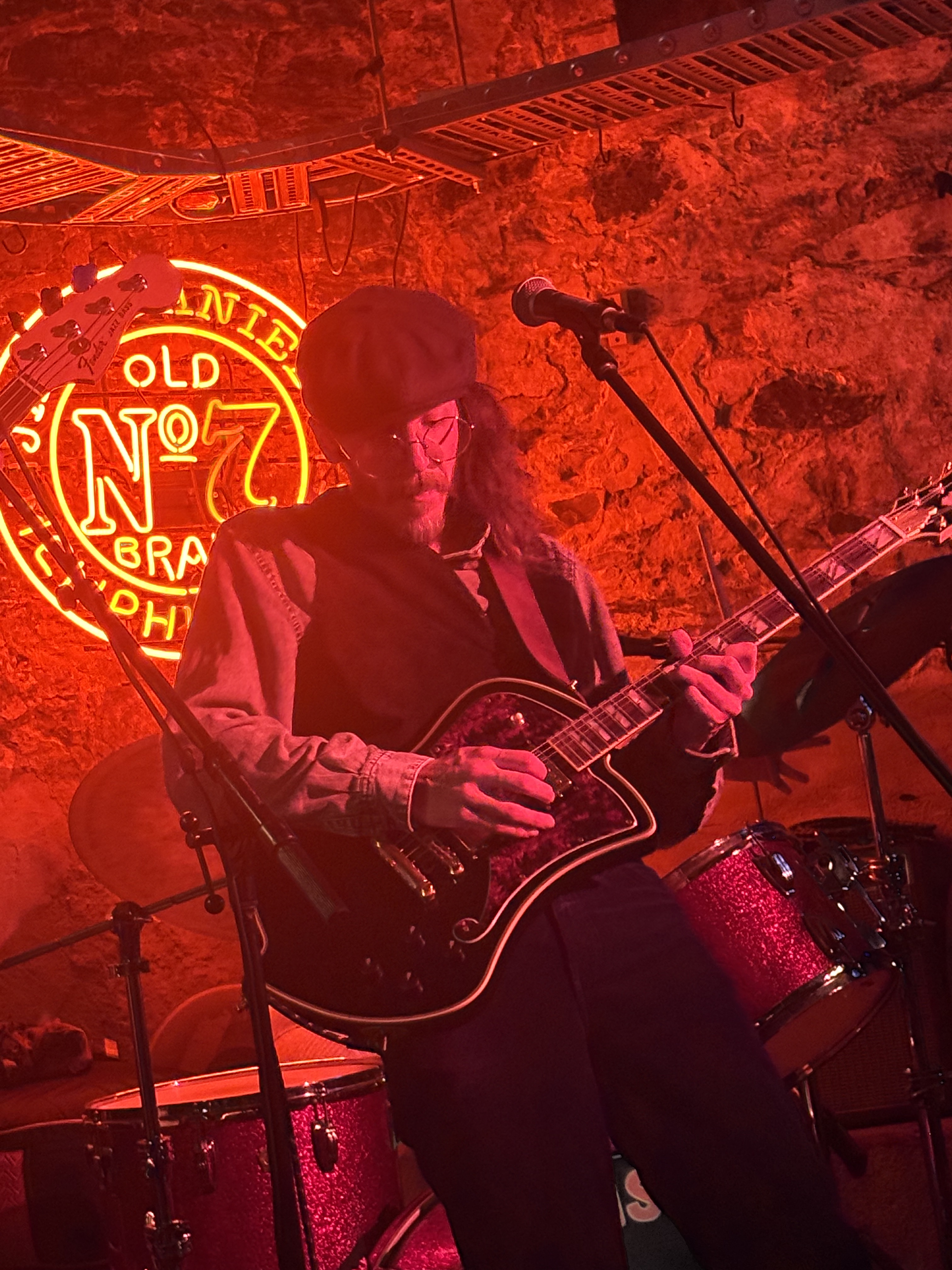 Jess Foenander performing guitar on stage under red neon lighting